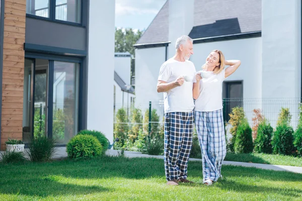 Esposa radiante y esposo usando pantalones de pijama cuadrados y zapatos de casa — Foto de Stock