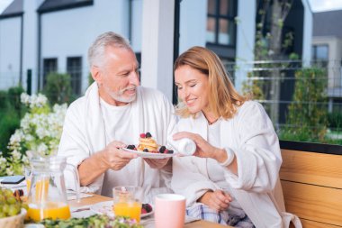 Sarışın karısı onu sabah krep yerken üzerine bazı Tepesi giyerken gülümseyen