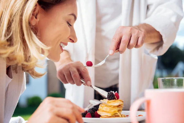 Amado marido vestindo pijama alimentando sua bela esposa loira — Fotografia de Stock