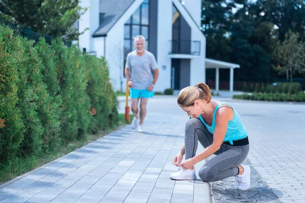 Fit ve ince sarışın işkadını çalıştırmadan önce spor ayakkabılarını bağlama — Stok fotoğraf