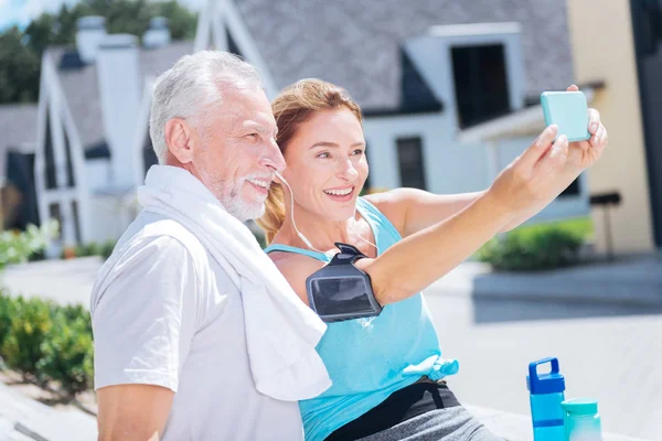 Sonriendo atractiva mujer sosteniendo el teléfono azul mientras toma una foto con su marido —  Fotos de Stock