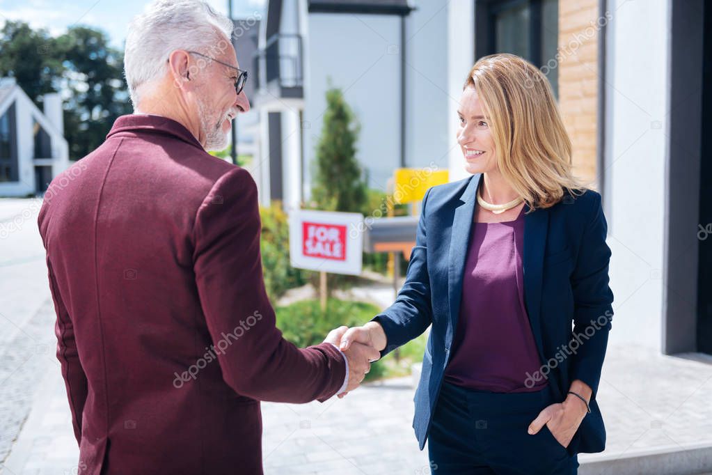 Bearded grey-haired prosperous man shaking hand of estate broker