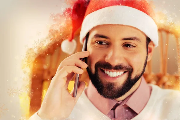 Бородатий усміхнений чоловік у новорічному капелюсі тримає срібний смартфон в руці — стокове фото