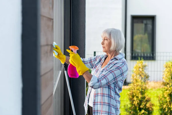 Mujer madura con guantes amarillos lavando ventanas de la casa de verano — Foto de Stock