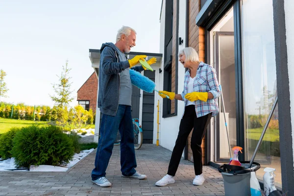 Modern laughing grandmother and grandfather having fun cleaning territory