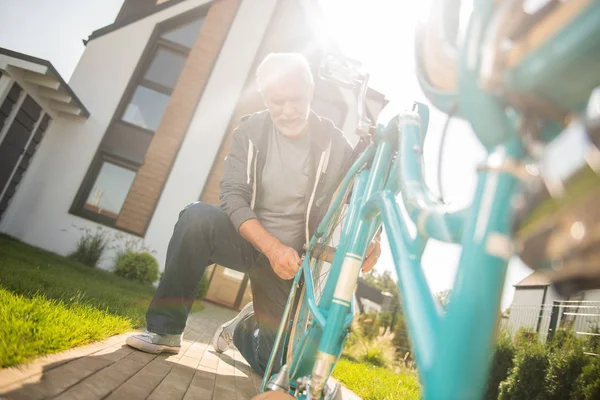 Hombre mayor moderno con zapatillas azules reparando su vieja bicicleta azul — Foto de Stock