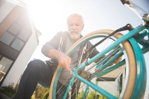 Бородатый старик в темных джинсах, занят ремонтом велосипеда. — стоковое фото