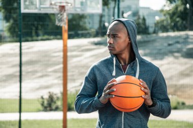 Bir basketbol topu tutan ciddi genç adam