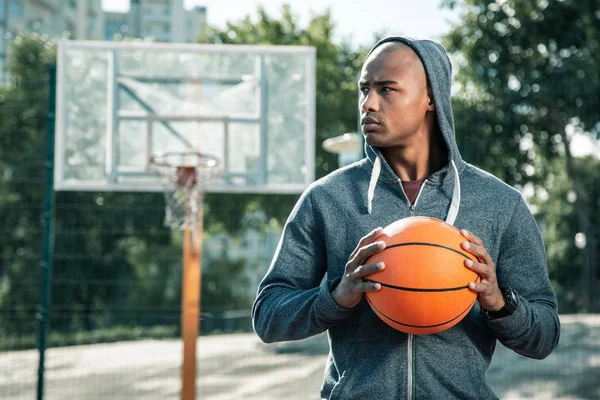 Ein ernsthafter junger Mann schaut auf den Basketballplatz — Stockfoto