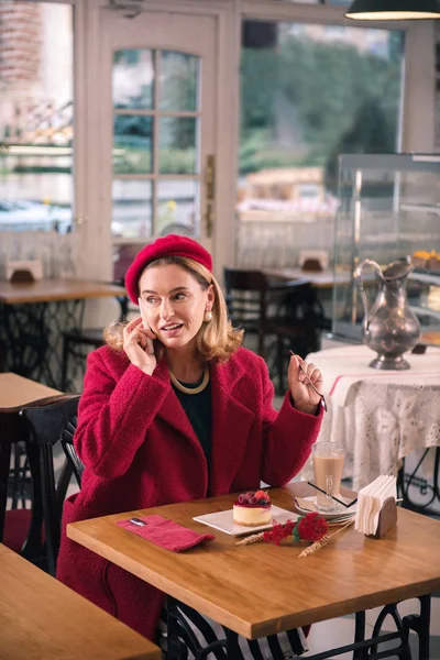 Elegant blonde-haired woman sitting in bakery while calling her friend — Stock Photo, Image