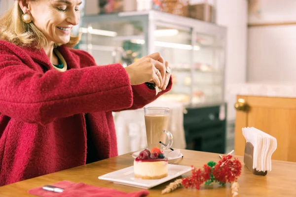 Lächelnde reife Frau mit Gesichtsfalten, die Zucker in ihren Kaffee gibt — Stockfoto