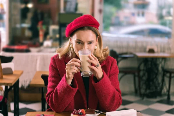 Elegant French woman wearing nice earrings drinking latte in cafeteria