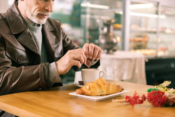 Szakállas ősz hajú ember visel cukor hozzáadása a kávé barna bőrkabát — Stock Fotó