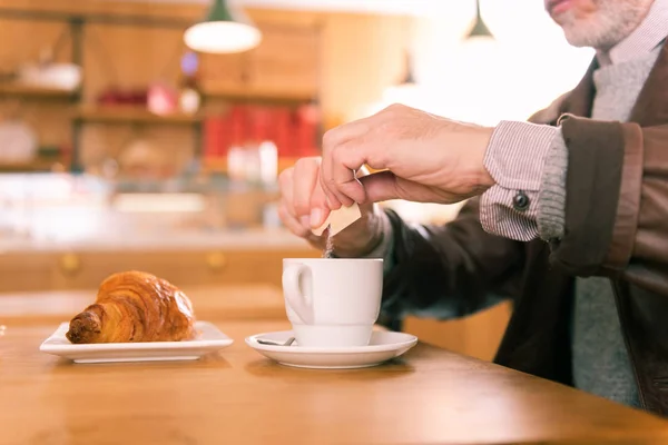 Bearded man spending morning in French bakery eating croissant