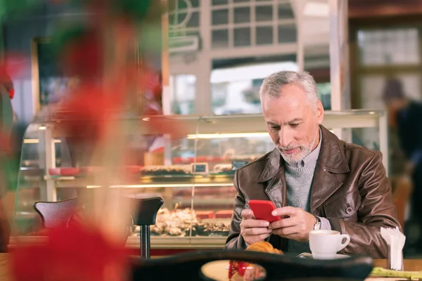 Mature French man feeling busy while checking working e-mail on phone