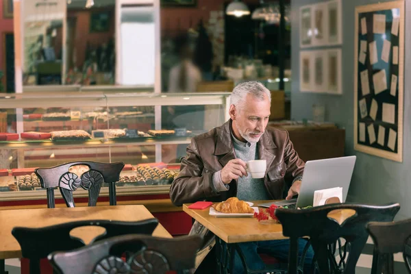 Famous writer writing novel using his laptop sitting in bakery