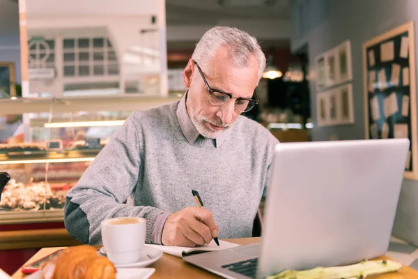 Grey-haired mature writer wearing glasses working using his laptop