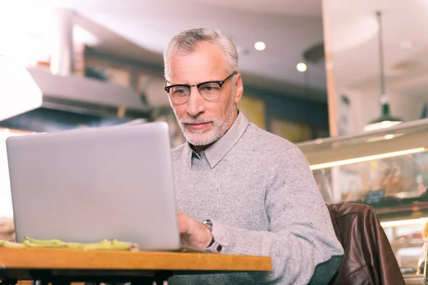 Bonito homem maduro vestindo camisola cinza trabalhando duro usando seu laptop — Fotografia de Stock