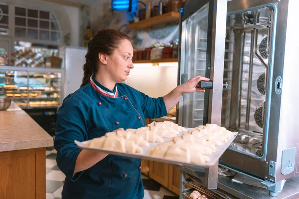 法国面包师穿着蓝色夹克, 把羊角面包放在烤箱里 — 图库照片