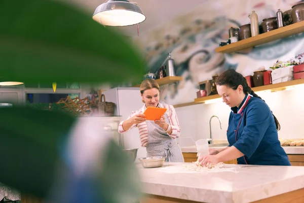 Beaming entrepreneur making video of her employee cooking croissants — Stock Photo, Image
