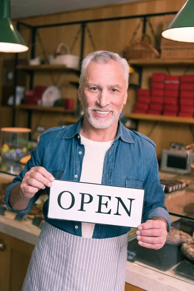 Empresário sorridente de cabelos grisalhos usando camisa jeans abrindo sua cafetaria — Fotografia de Stock