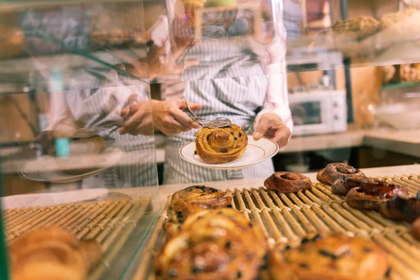 Frau arbeitet in Cafeteria und stellt Zimtbrötchen ins Schaufenster — Stockfoto