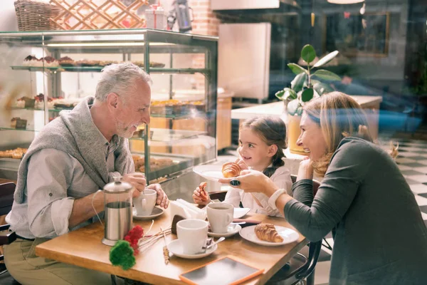 Grandfather smiling. Bearded grey-haired grandfather smiling looking at his cute appealing girl having breakfast together