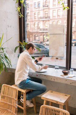 Şık erkek kot pantolon ve beyaz gömlek atmosferik Vejeteryan kafede oturan giymiş
