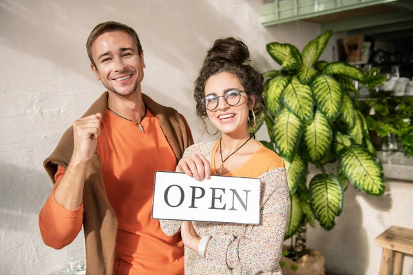 Красивая жена в очках, стоящая рядом со своим мужчиной, открывающим кафе вместе — стоковое фото