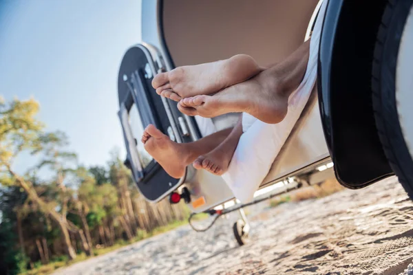 Couple of barefooted travelers lying in their compact trailer standing near beach — Stock Photo, Image