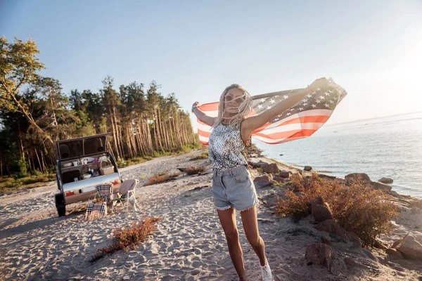 Stylish woman with dreadlocks wearing sunglasses holding American flag