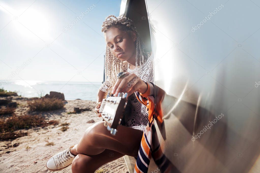 Stylish musician wearing scarf on her hand playing the guitar sitting in trailer