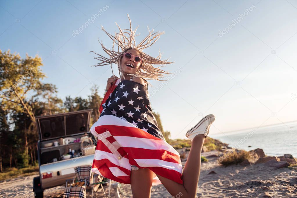 Cheerful woman holding American flag jumping high feeling happy
