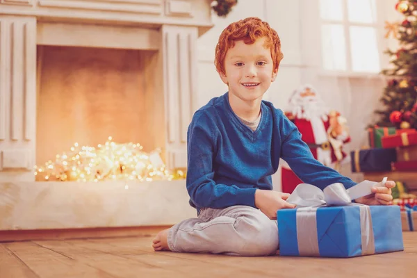 Очаровательный мальчик позирует с рождественским подарком на полу — стоковое фото