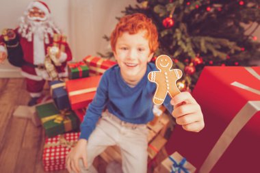 Neşeli çocuk Noel ağacı yanında otururken zencefilli kurabiye adam gösterilen