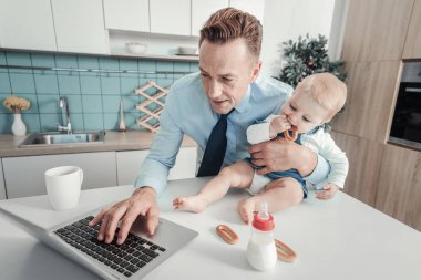 Bir nursling sarılma ve dizüstü bilgisayar kullanarak hoş meşgul adam.