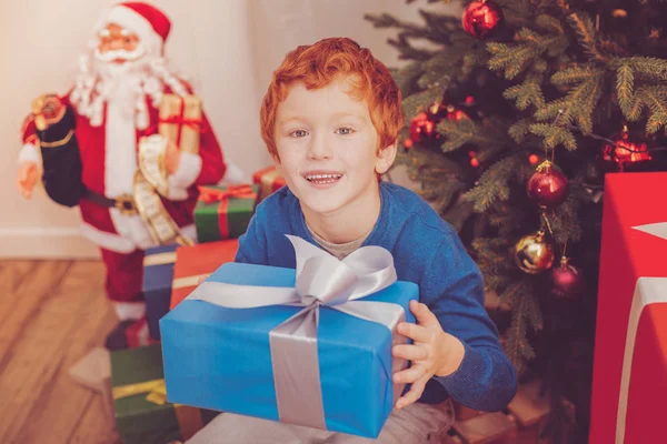 Рыжий мальчик сидит под елкой с подарком — стоковое фото