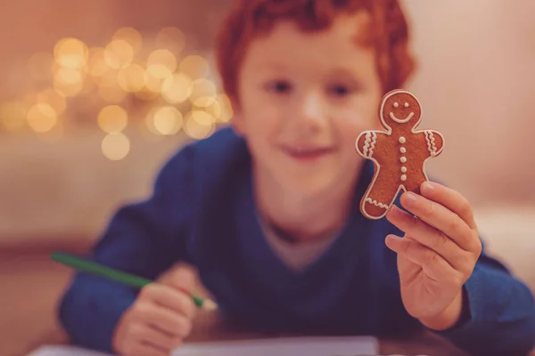Red-haired boy showing gingerbread man while drawing it