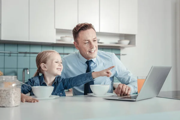 Interesse vreugdevolle meisje zittend en wijzend op de laptop. — Stockfoto