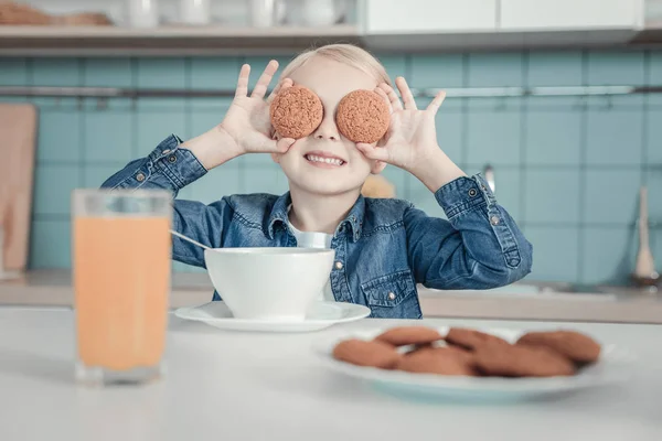 Happy smiling girl hiding eyes by cookies and having breakfast. — Stock Photo, Image