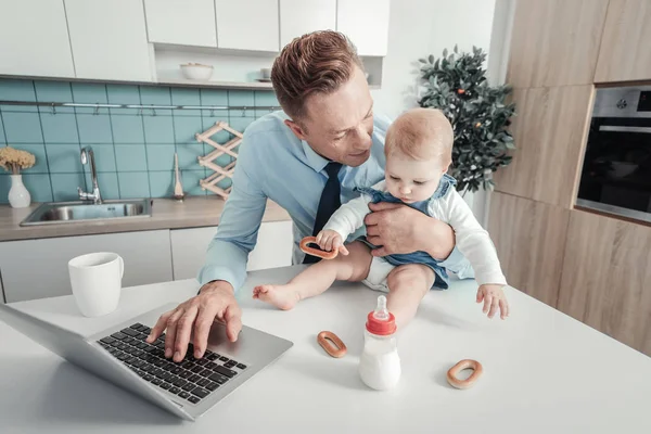Cuidar padre encantador usando el portátil mirando al bebé . — Foto de Stock