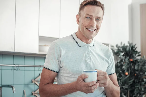 Angenehmer gutaussehender Mann, der lächelt und eine Tasse hält. — Stockfoto