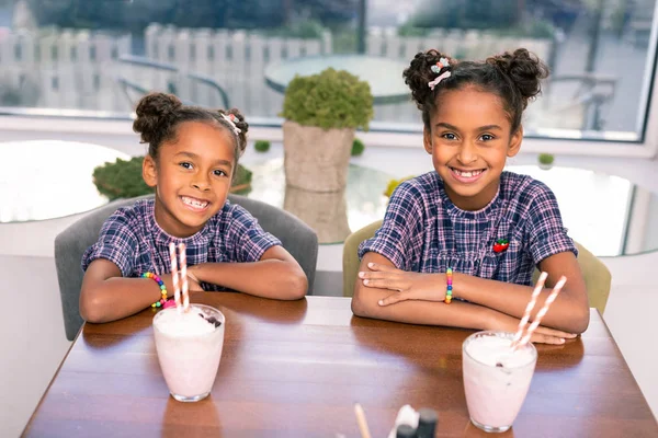 Dos hermanos radiantes lindos sentados en la cafetería bebiendo cóctel de leche —  Fotos de Stock