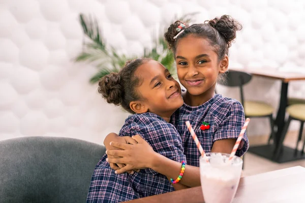 Cariñosa hermana mayor abrazando a su linda hermana pequeña usando vestido cuadrado —  Fotos de Stock