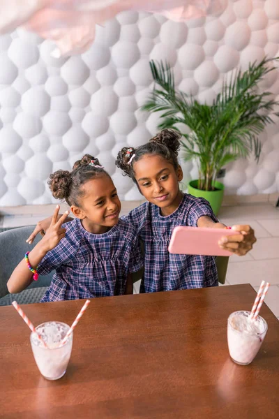 Hermana mayor sosteniendo su teléfono inteligente rosa haciendo foto con su hermana —  Fotos de Stock