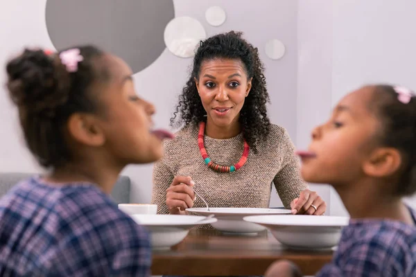 Dark-eyed mother feeling overwhelmed watching her daughter playing tricks