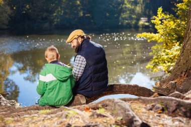 Güzel pozitif adam ve ağaç kök üzerinde oturan çocuk