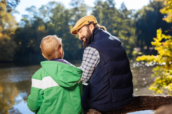 うれしそうな幸せな父と息子が湖の近くに座って — ストック写真