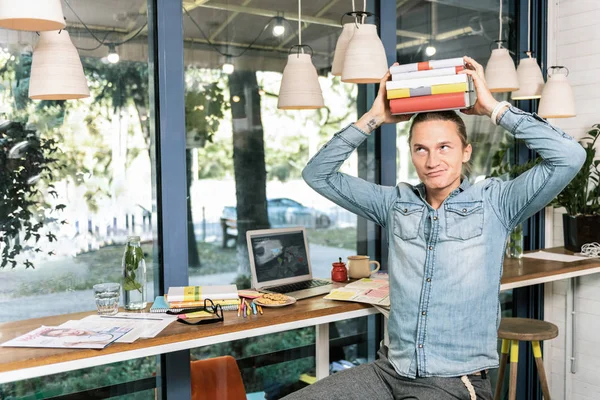 Angenehmer junger Mann legt Bücher auf den Kopf — Stockfoto