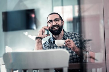 Biraz kahve yudumlarken Telefonla konuşan sakallı adam gülümseyen